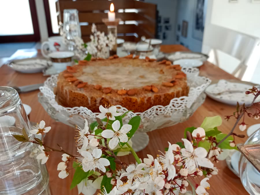 Selbst gebackener Mandelkuchen auf Glas-Etagere, gedeckter Tisch mit Kirschblüten